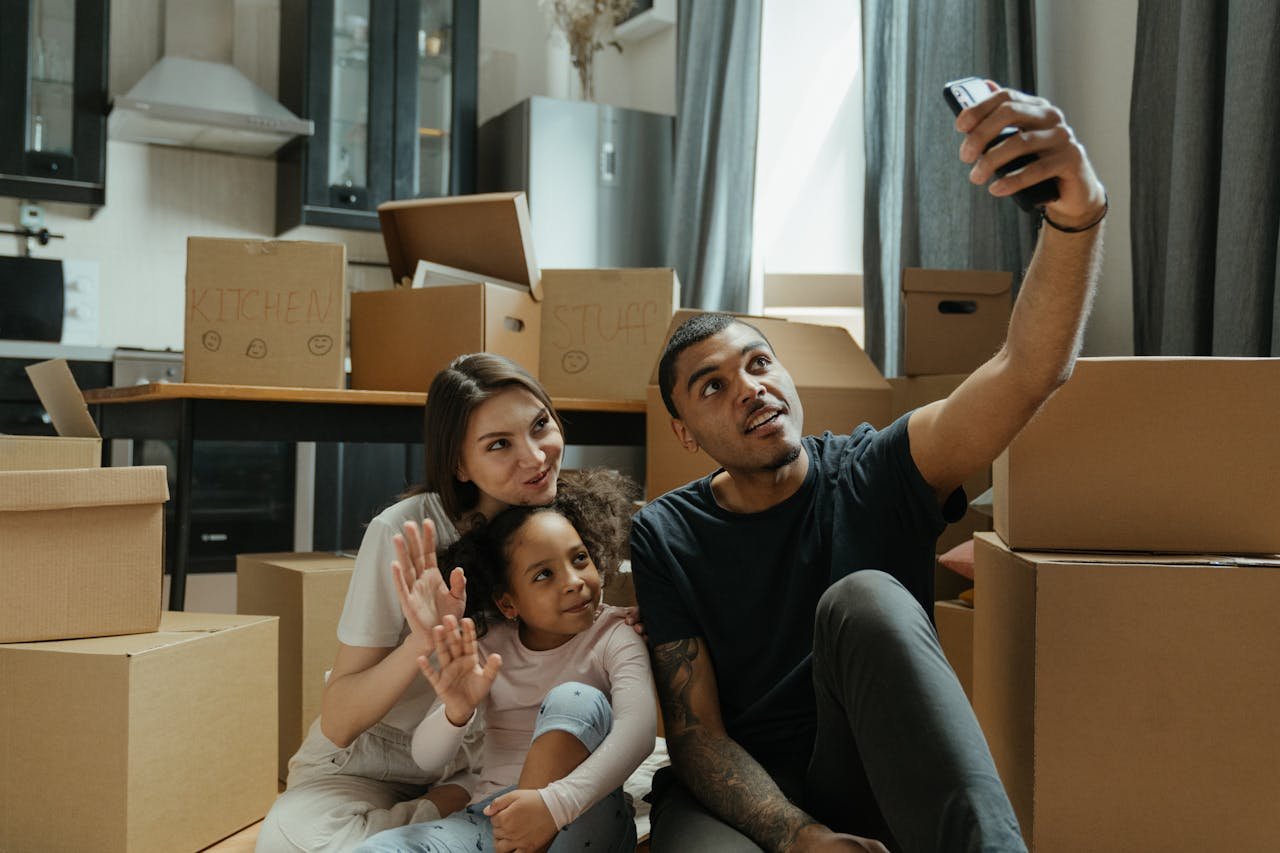 A cheerful family takes a selfie while surrounded by moving boxes in their new home.
